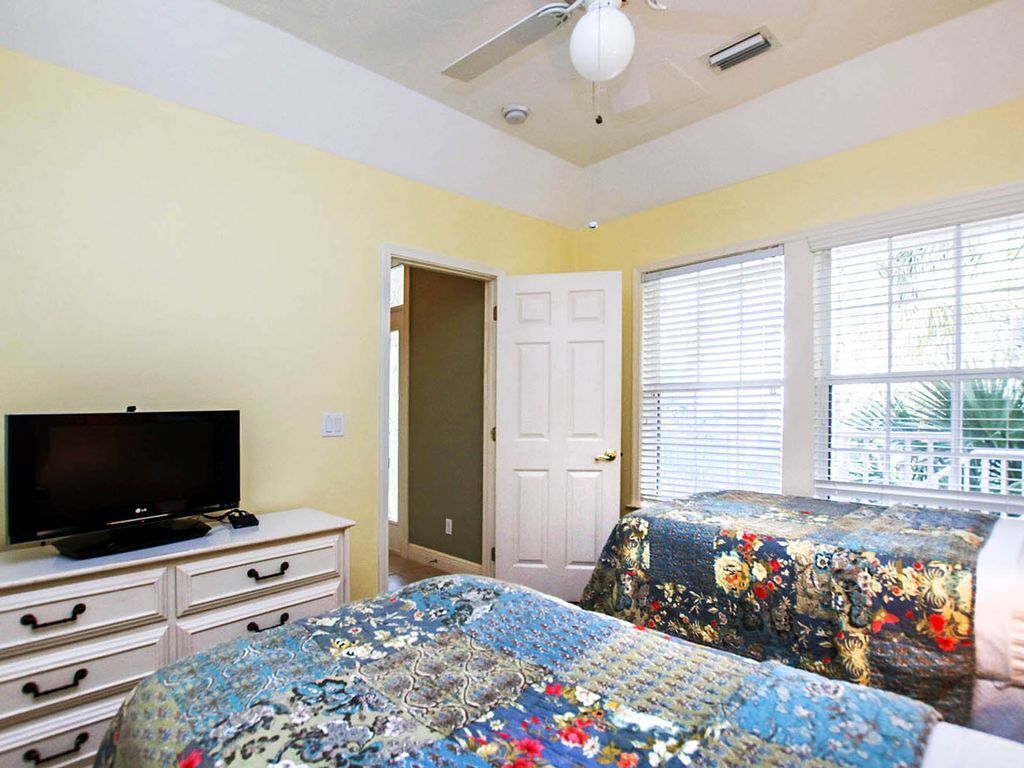 A bedroom with a bed, a TV, a ceiling fan, and a window with blinds.