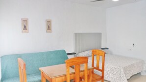 A room with a teal sofa, a wooden table with two chairs, a bed with patterned bedding, and a ceiling fan. - Two person apartment in ideal location (Conil de la Frontera)