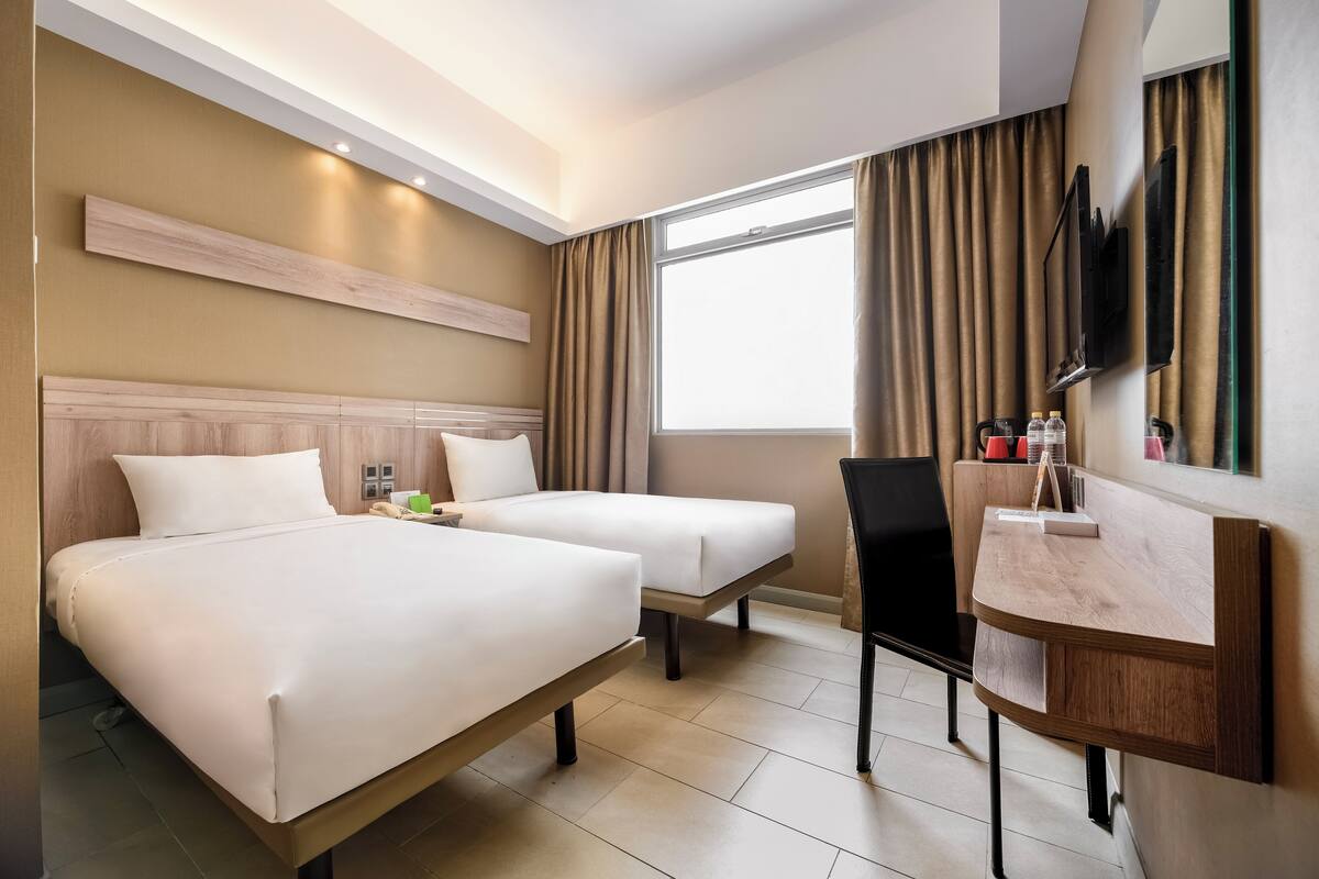 Une chambre d’hôtel avec deux lits, un bureau, une chaise, une télévision et une fenêtre avec des rideaux.