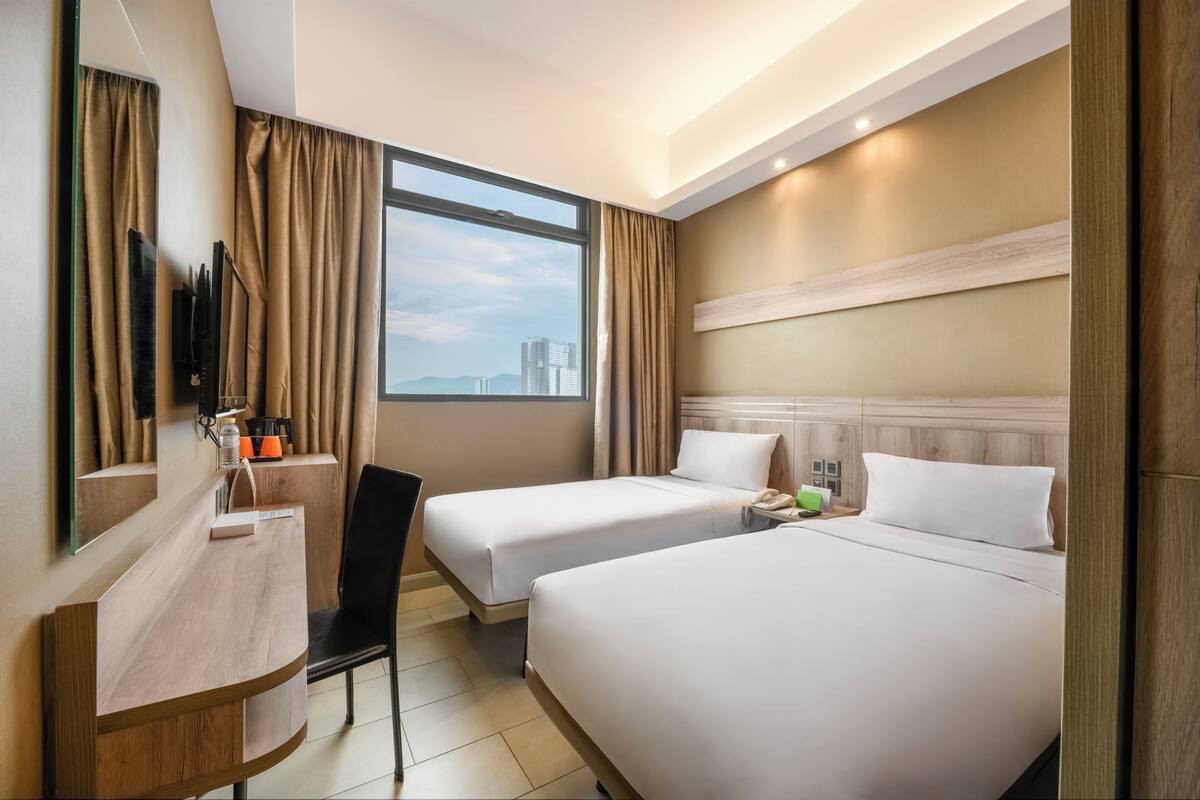 Une chambre d’hôtel avec deux lits, un bureau, une chaise, une télévision et une fenêtre donnant sur la ville.