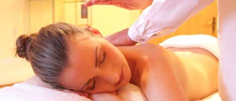 A person receiving a massage in a room with a white bed and a white towel.