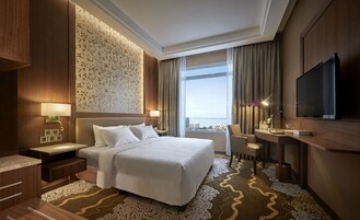 Habitación de hotel con una cama grande, un escritorio con silla, televisión y vistas a la ciudad.