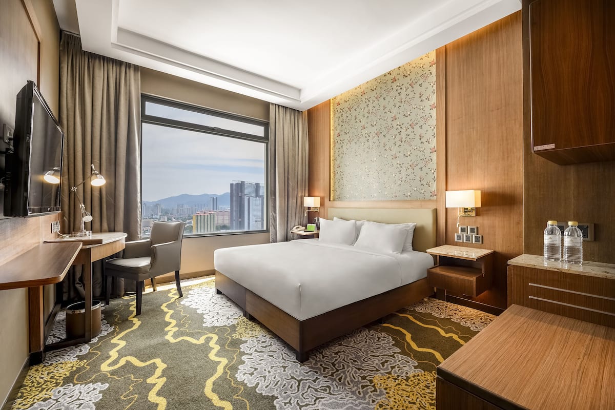 Een hotelkamer met een groot bed, een bureau met stoel, een televisie en uitzicht op een stadsgezicht door een groot raam.