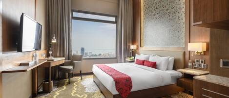 Habitación de hotel con una cama grande, un escritorio, una silla, un televisor y vistas a la ciudad.