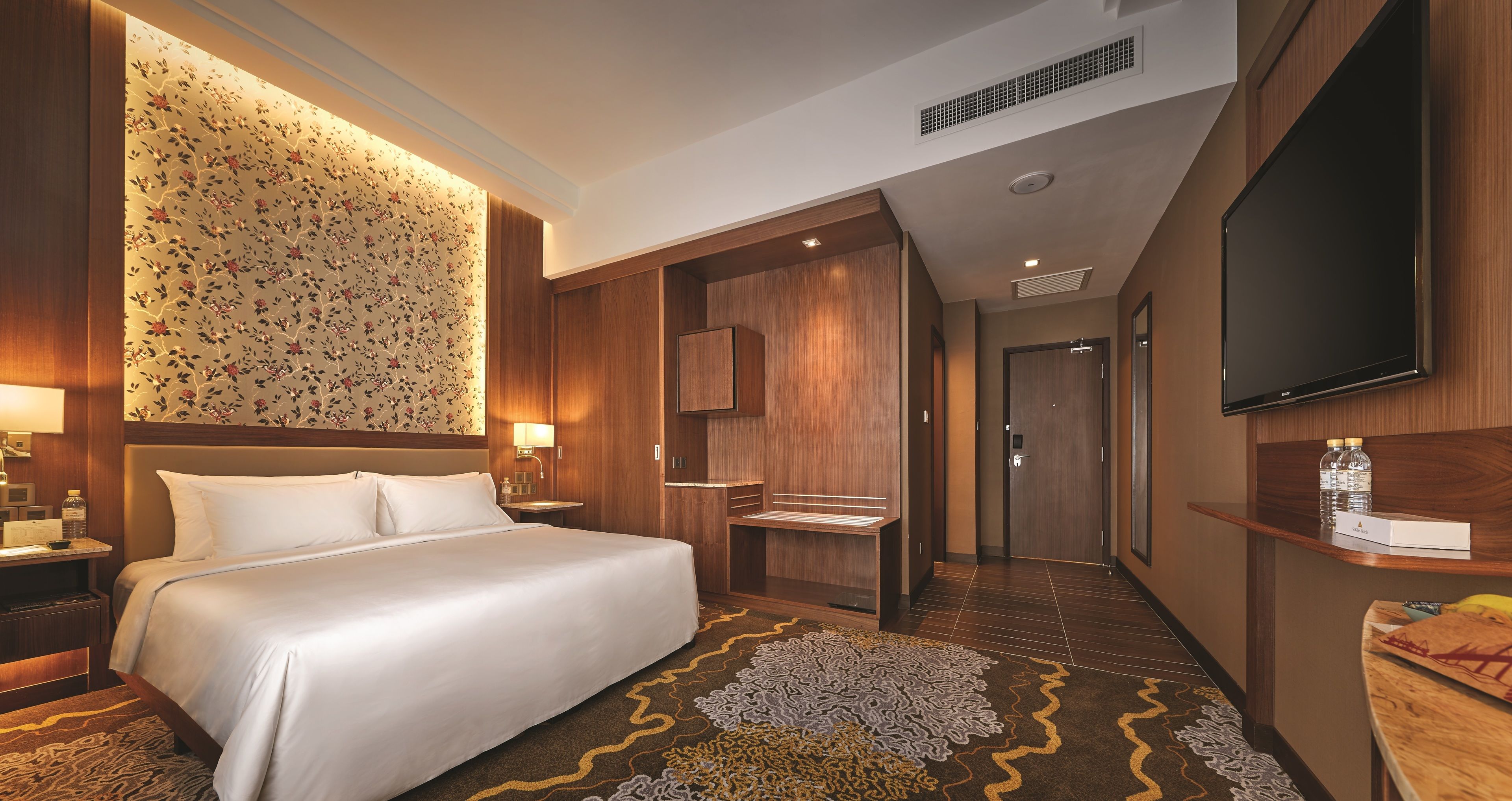 Ein Hotelzimmer mit einem großen Bett, einem Schreibtisch mit Lampe, einem Fernseher und einem Badezimmer mit Spiegel und Toilette.
