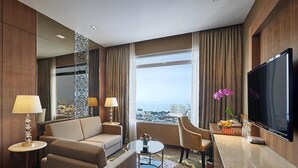 Een hotelkamer met een bank, fauteuils, een salontafel, een televisie en uitzicht op de stad.