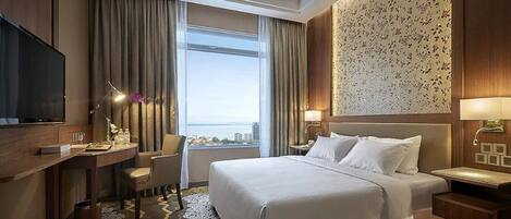Habitación de hotel con una cama grande, un escritorio con silla, televisión y vistas a la ciudad desde la ventana.