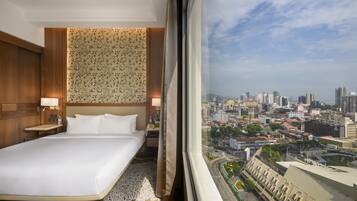A hotel room with a large bed, a nightstand, a lamp, and a view of a cityscape through a window.