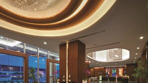 Een moderne lobby met een grote kroonluchter, een receptiebalie en uitzicht naar buiten.