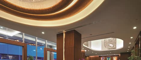 A modern lobby with a large chandelier, a reception desk, and a view of the outside.