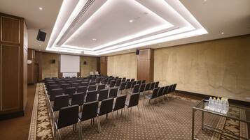 A conference room with rows of chairs, a projector screen, and a table with water bottles.