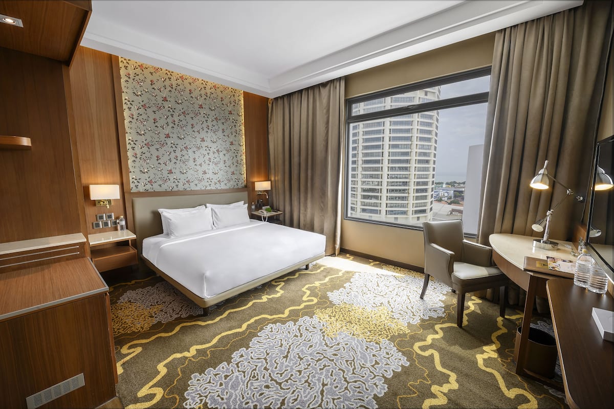 Hotelkamer met een groot bed, een bureau, een stoel, een bureaulamp, een nachtkastje, een spiegel en een raam met uitzicht op de stad.