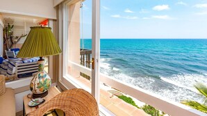 Uma varanda com vista para o oceano, uma cadeira de vime, uma mesa com abajur e um sofá com almofadas listradas.