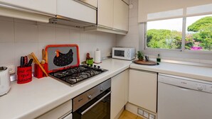 Cozinha moderna com armários brancos, fogão a gás, micro-ondas e janela com vista para o verde.