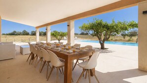 An outdoor dining area with a pool view, wooden table, white chairs, and a clear sky. - Wonderful private villa for 12 people with A/C, private pool, WIFI, TV, patio and panoramic view (Costitx)