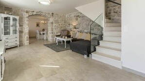 A spacious living area with a stone wall, a glass staircase, and a dining area with a chandelier.