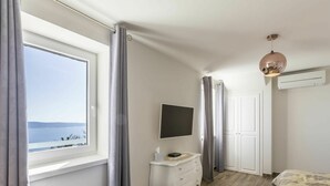 A bedroom with a large window, a bedside table, a TV, a wardrobe, and a bed with a patterned bedspread.