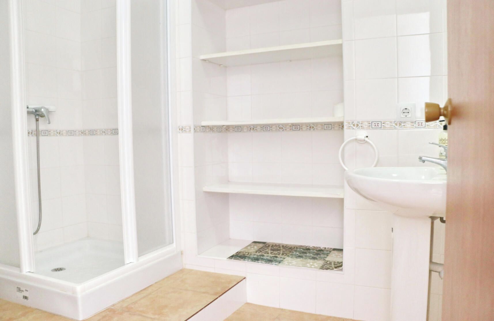 Un baño con ducha, lavabo y piso de baldosas.