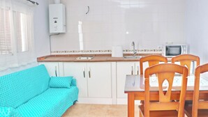Una cocina compacta con muebles blancos, una mesa de comedor de madera y un sofá color turquesa.