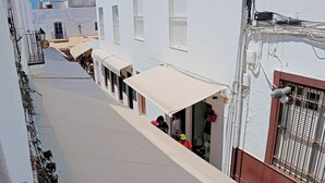 Una calle estrecha con edificios blancos, un corredor cubierto y una ventana con celosía de metal.