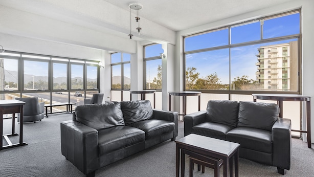 A spacious lounge area with leather sofas, a coffee table, and a view of a cityscape through large windows. - Rockhampton Riverside Central Hotel (Rockhampton)