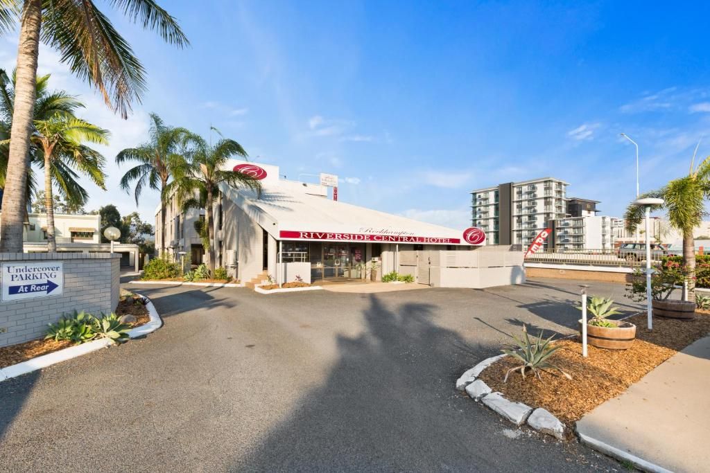 A hotel entrance with a sign for Riverside Central Hotel, a parking area, and palm trees.