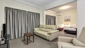 A hotel room with a beige sofa, a small wooden table, a bed with a dark headboard, and a painting on the wall. - Rockhampton Riverside Central Hotel (Rockhampton)
