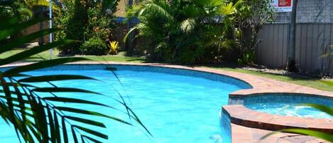 A swimming pool with a curved edge, surrounded by lush greenery and a wooden fence.