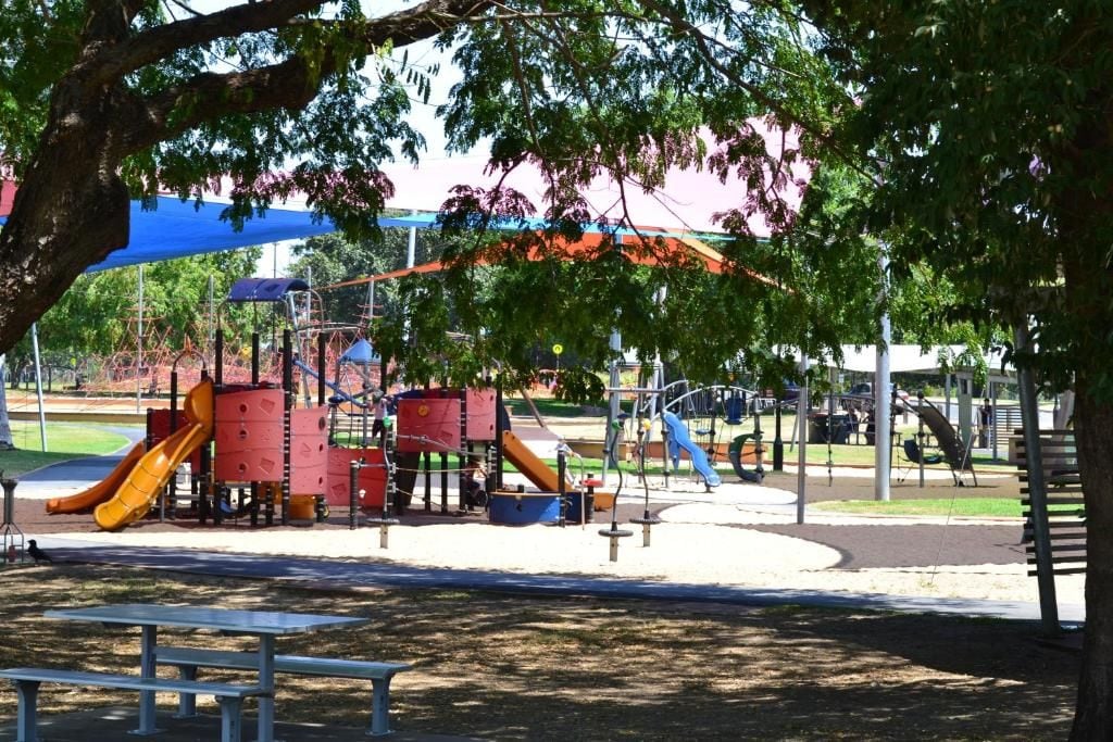A playground with slides and climbing structures, surrounded by trees and benches.