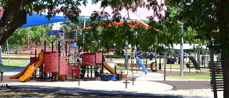 Un parque infantil con toboganes y estructuras para escalar, rodeado de árboles y bancos.