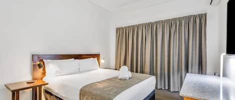 A hotel room with a bed, a nightstand, a desk, a TV, and a window with curtains.