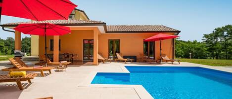 Une maison moderne dotée d’une piscine, d’un espace salon extérieur et de parasols rouges.