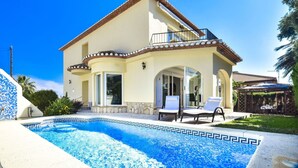 Una casa de dos pisos con piscina, un balcón y un patio con sillas de descanso.