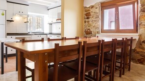 A modern kitchen with white cabinets, a wooden dining table, and a stone wall. - Ruralsurf - Hostel (Castrillon)