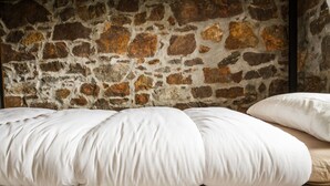 A bed with white bedding against a stone wall. - Ruralsurf - Hostel (Castrillon)