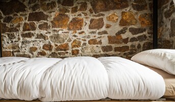 A bed with white bedding against a stone wall.