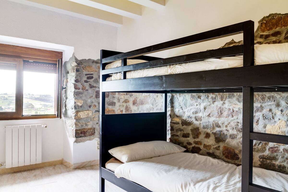 A bunk bed room with a stone wall and a window overlooking a landscape.