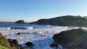 A coastal landscape with rocky shores, waves, and a grassy hill. - Ruralsurf - Hostel (Castrillon)
