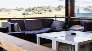 A balcony with a sofa and tables, offering a view of a rural landscape. - Ruralsurf - Hostel (Castrillon)