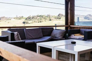 A balcony with a sofa and tables, offering a view of a rural landscape.