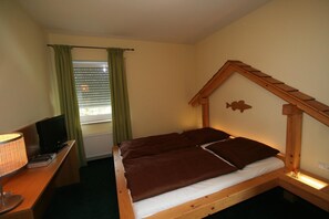 A single bed with a wooden headboard, a desk with a lamp, and a television. - Gästezimmer Fischerstüberl (Windorf)