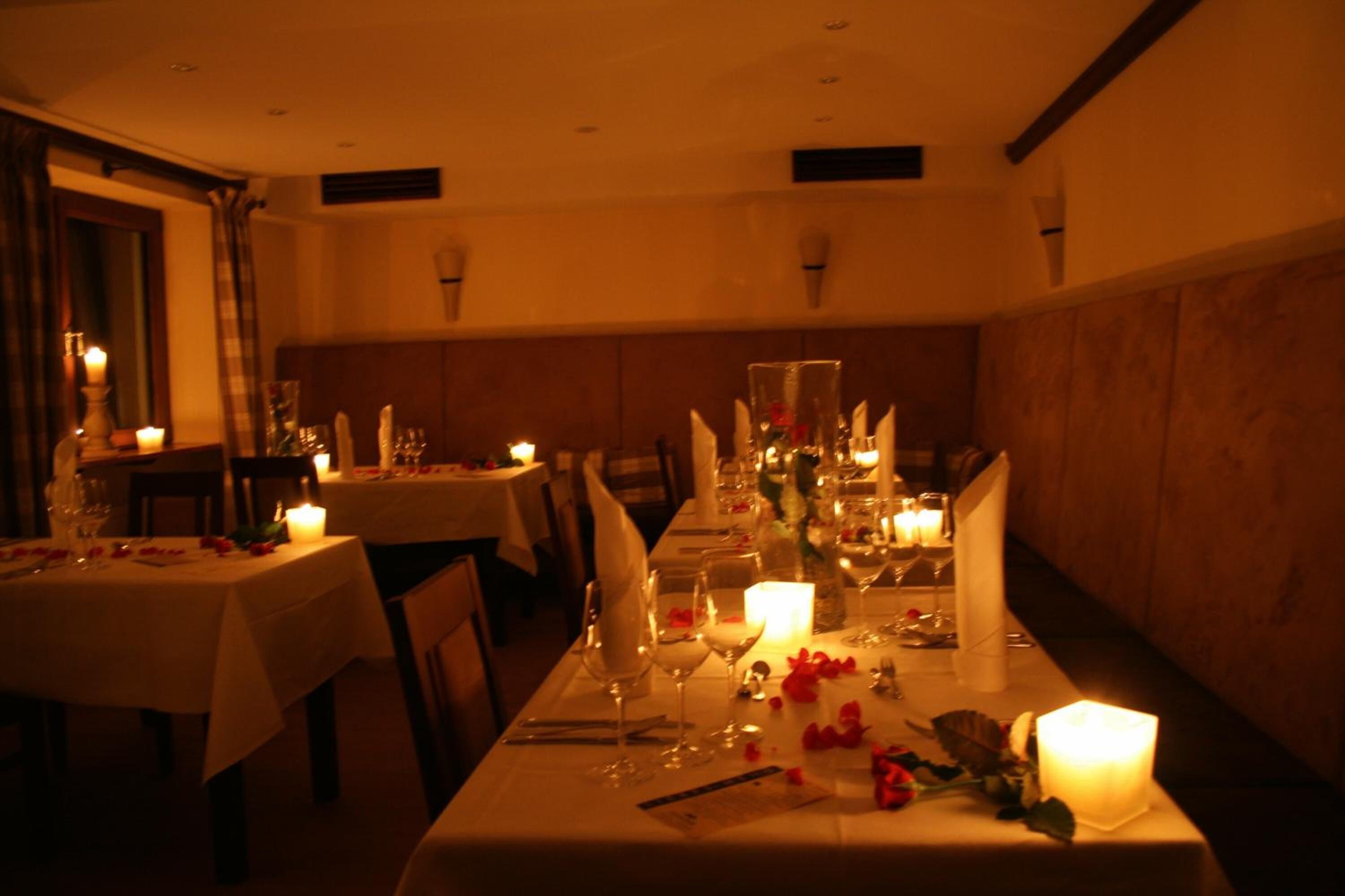 A dimly lit dining area with tables set for a meal, candles, and floral decorations.
