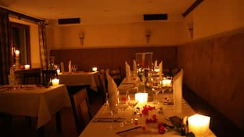 A dimly lit dining area with tables set for a meal, candles, and floral decorations.