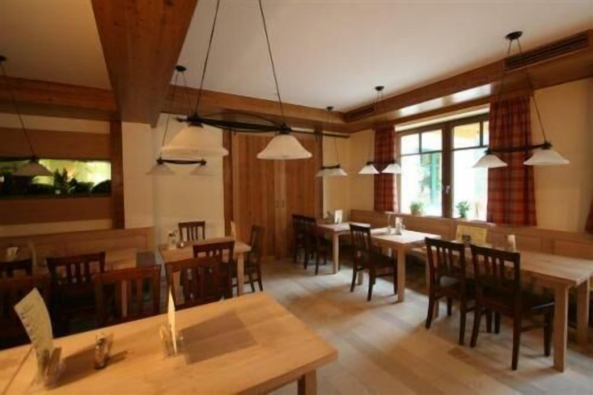 Un comedor amplio con mesas y sillas de madera, iluminación colgante y ventanas grandes con cortinas.