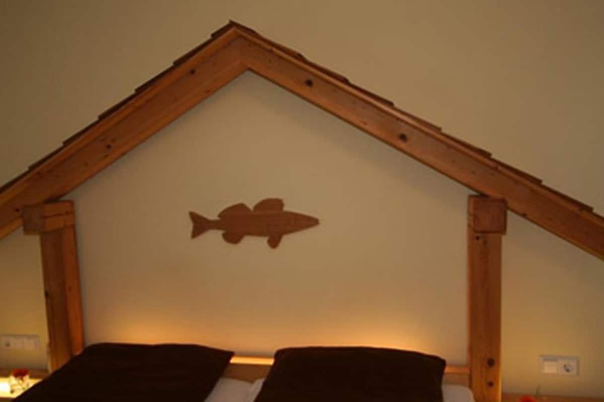 A bedroom with a wooden headboard shaped like a house, a fish silhouette on the wall, and a bedside table with a lamp.