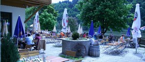 An outdoor seating area with tables and chairs, umbrellas, and a central wheel feature. - Gästezimmer Fischerstüberl (Windorf)