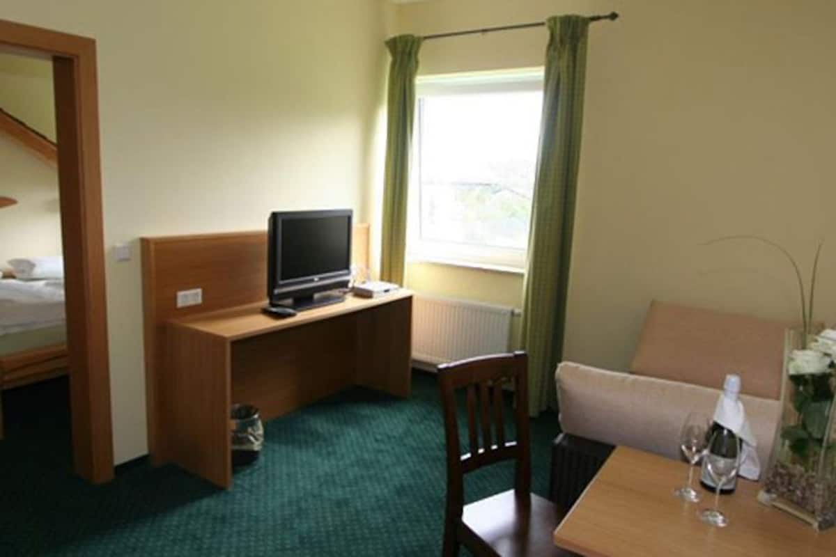 A hotel room with a bunk bed, a desk with a computer, a small table with a vase, and a window with curtains.