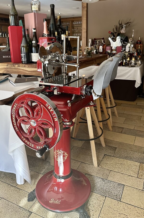 A vintage wine press with a red base and wheel, surrounded by bottles and glasses on a wooden table. - Gästezimmer Fischerstüberl (Windorf)