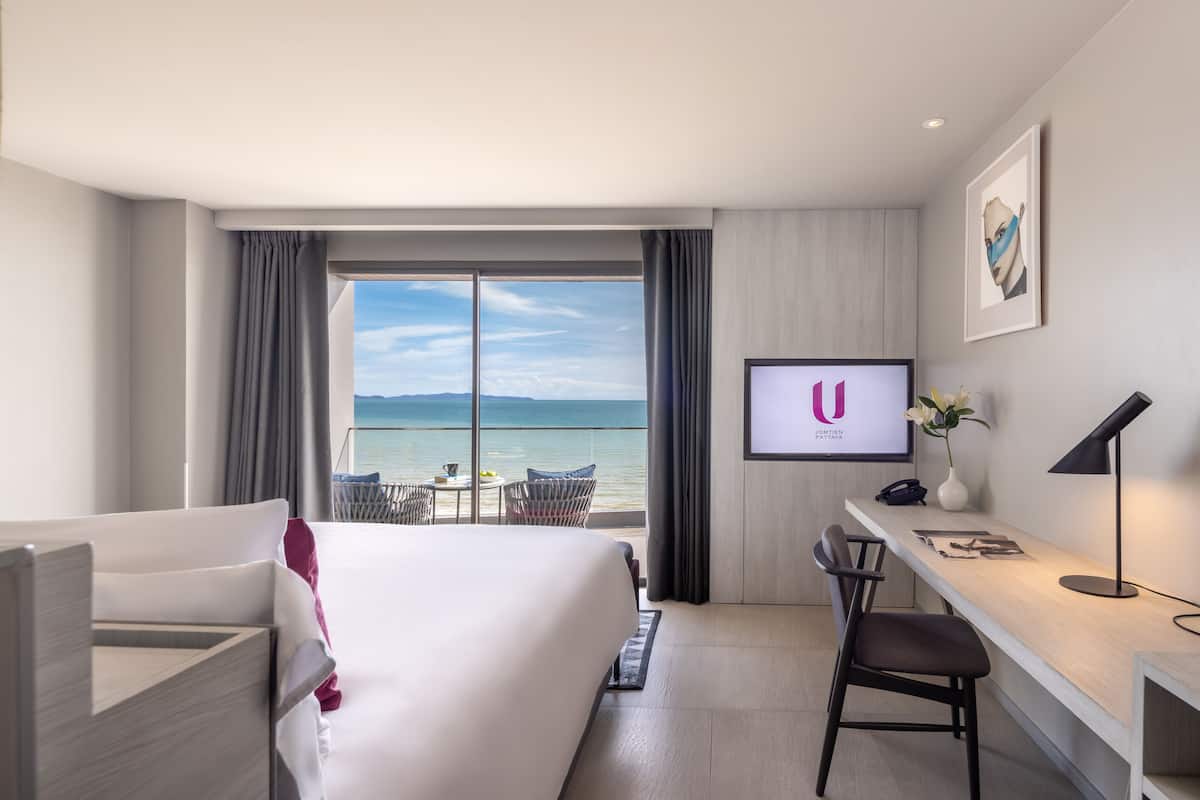 Habitación de hotel con cama, escritorio, silla, televisor y vista al mar.