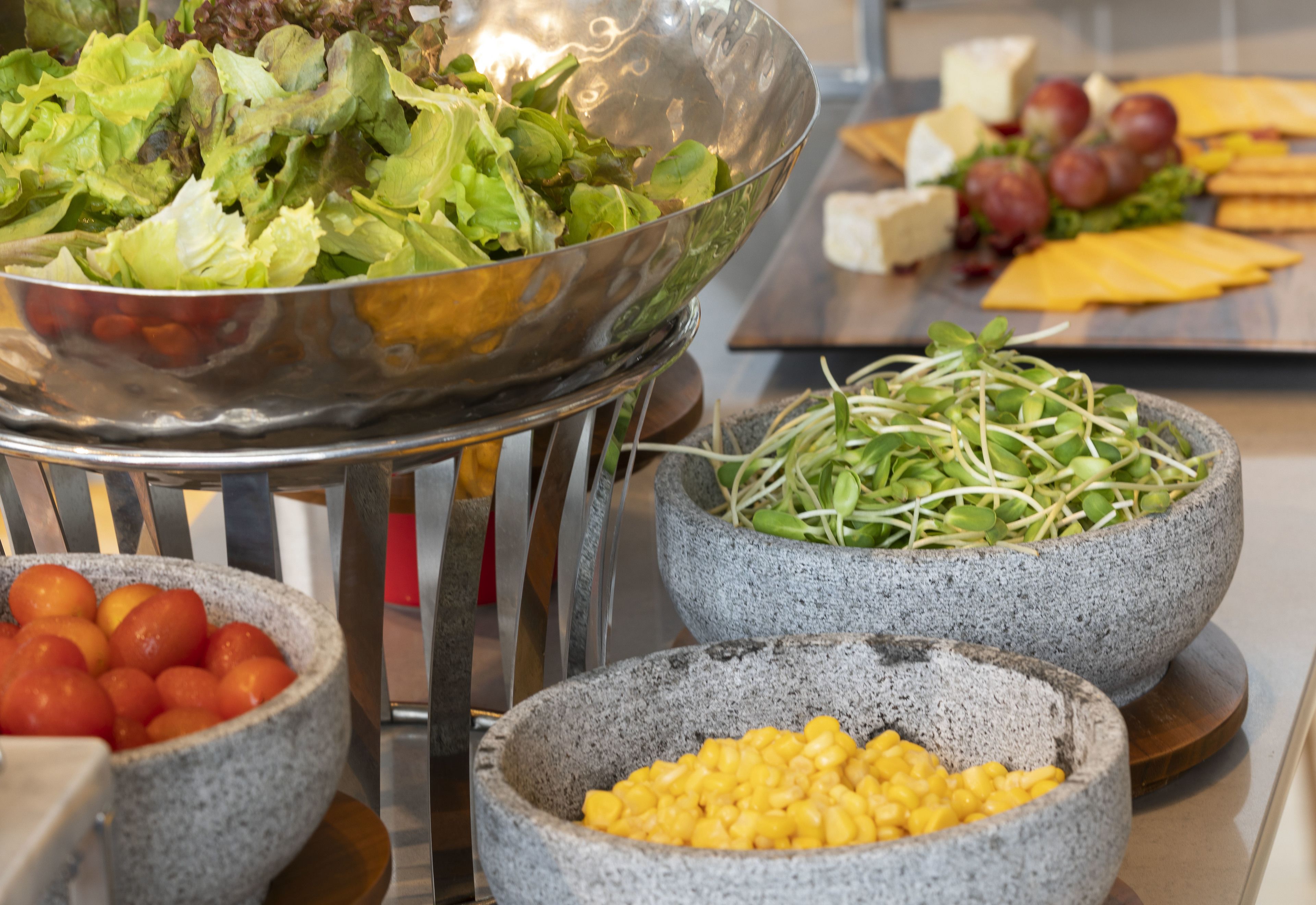 A buffet with various food items including a salad, cheese, grapes, and corn.